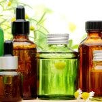 Image of a pretty collection of jars with essential oils in them. In the background there us freshly picjed cammomile flowers and shrub